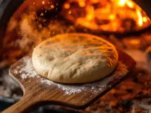 Pizzadeeg wordt op houten schep in professionele pizzaoven met vlammen geplaatst, met stoom en meeldeeltjes in lucht