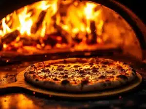 Napolitaanse pizza op houten schep wordt in professionele pizzaoven met hoge temperatuur en vlammen geschoven