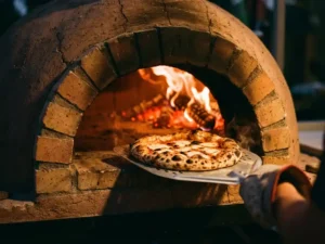 Napolitaanse pizza met perfect verkoolde korst wordt uit houtgestookte oven met gloeiende sintels getrokken
