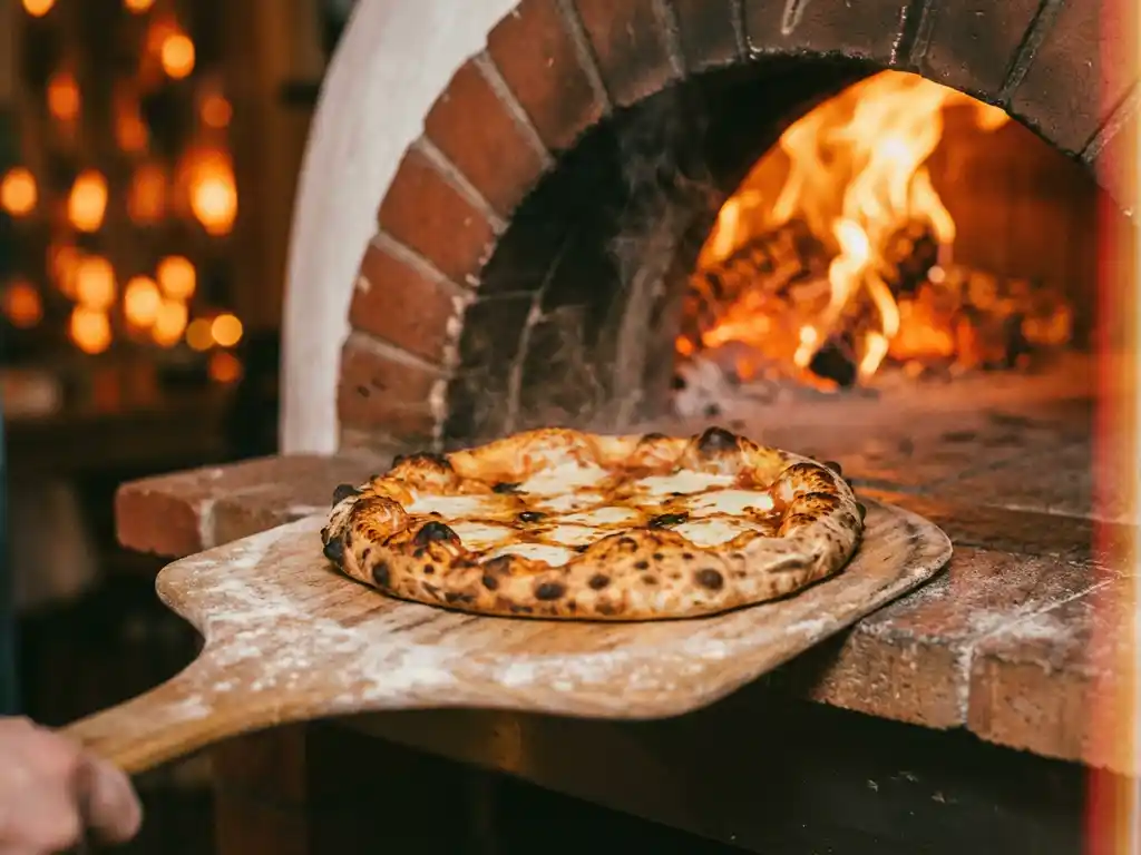 Napolitaanse pizza met goudbruine korst en borrelende mozzarella wordt uit een houtgestookte oven met oranje vlammen gehaald